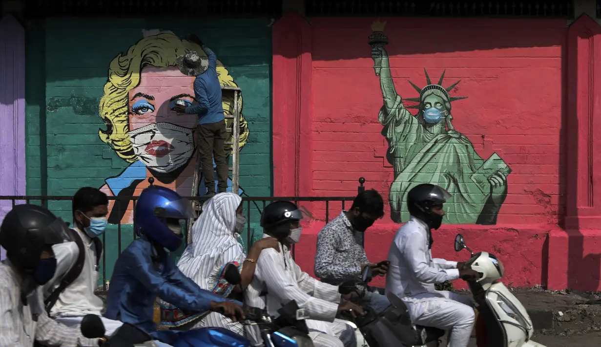 Seorang seniman melukis mural Marilyn Monroe, di samping salah satu Patung Liberty yang memakai masker untuk menyebarkan kesadaran akan pencegahan virus corona di Mumbai, India (26/3/2021). India telah melaporkan jumlah kasus virus corona tertinggi dalam empat bulan. (AP Photo/Rajanish Kakade)