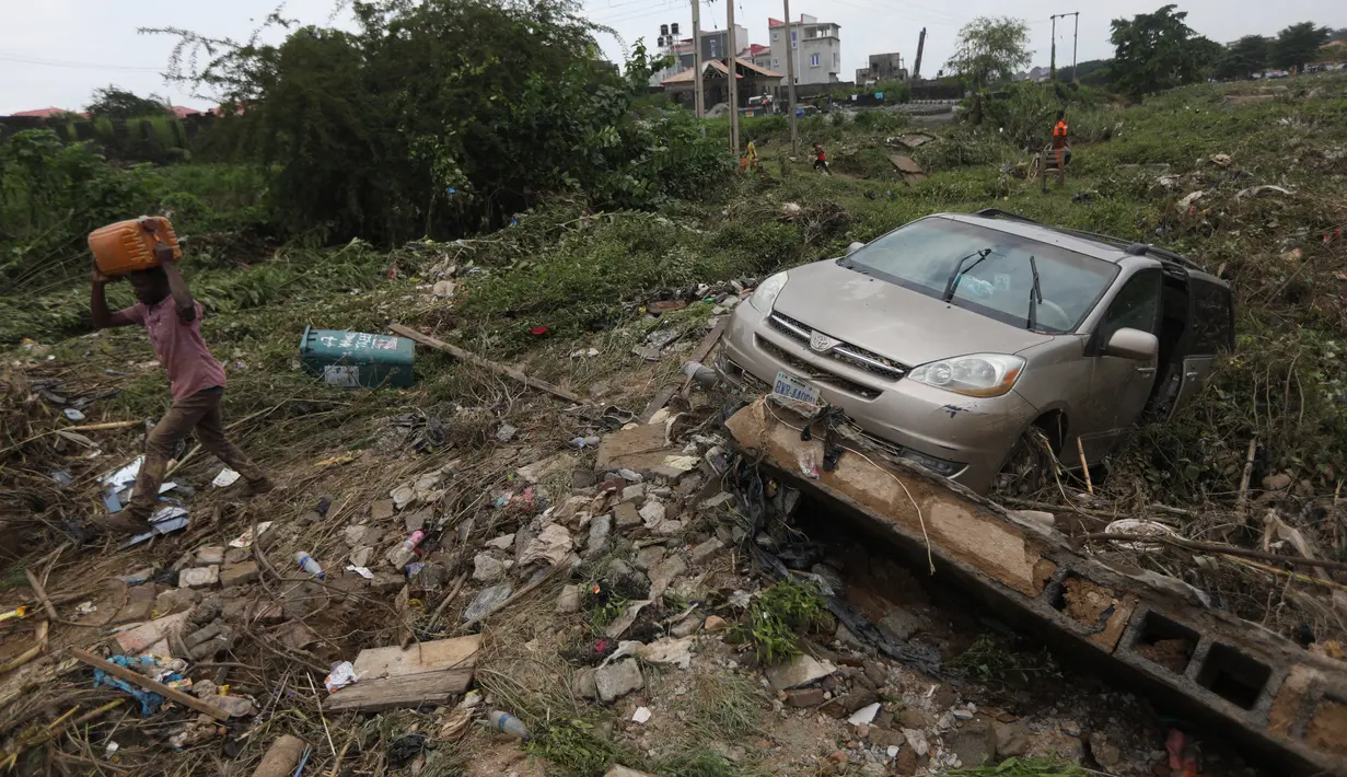 Seorang pria berjalan melewati kecelakaan mobil setelah hujan deras di Trademoore Estate, Lugbe, Abuja, Nigeria (13/9/2021). Badan Manajemen Darurat Nasional Nigeria (NEMA) mengkonfirmasi 3 orang tewas, dan puluhan mobil dan rumah terkena dampak di malapetaka. (AFP/Kola Sulaimon)