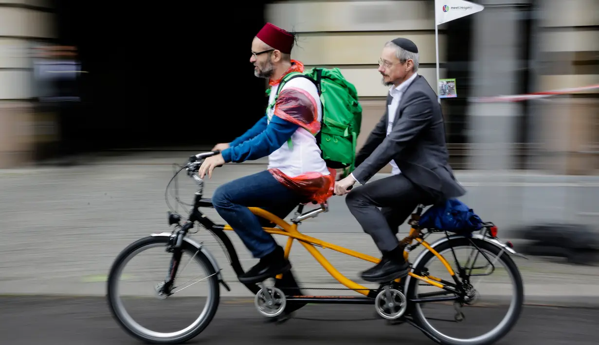 Seorang Muslim dan pria Yahudi mengayuh sepeda dengan berboncengan sebagai kampanye lintas agama melintasi Ibu Kota Jerman, Berlin, 24 Juni 2018. Aksi lintas iman ini untuk melawan kebencian atas nama agama di negara tersebut. (AP Photo/Markus Schreiber)