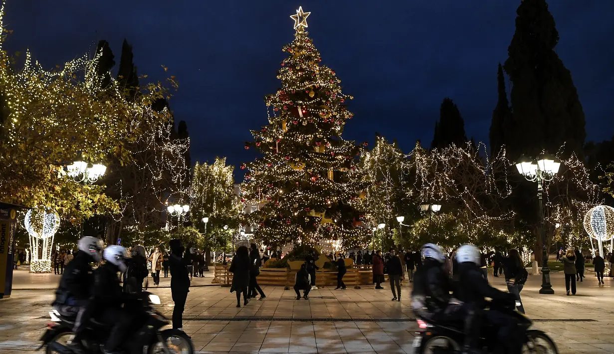 Polisi berpatroli dengan sepeda motor di alun-alun Syntagma yang diterangi dekorasi Natal di pusat kota Athena, Yunani pada 21 Desember 2020. Yunani akan merayakan musim Natal di bawah langkah-langkah penguncian wilayah atau lockdown COVID-19 hingga 7 Januari 2021 mendatang. (LOUISA GOULIAMAKI/AFP)