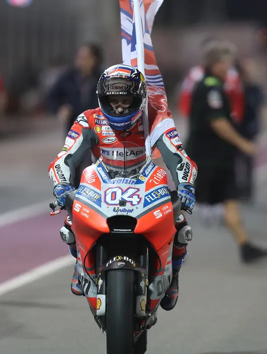 Pembalap Ducati Andrea Dovizioso mengendarai motornya sambil membawa bendera usai memenangkan balapan MotoGP Qatar 2018 di Sirkuit Internasional Losail (18/3). Andrea Dovizioso sukses memenangi seri pembuka MotoGP 2018 di Qatar. (AFP Photo/Karim Jaafar)