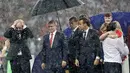 Presiden FIFA Gianni Infantino menutupi kepalanya dengan tangan sementara Presiden Rusia, Vladimir Putin dilindungi payung saat hujan turun selama penyerahan medali dan trofi Piala Dunia 2018 di Stadion Luzhniki, Minggu (15/7). (AP/Matthias Schrader)