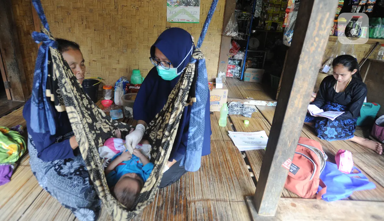 Petugas medis Puskesmas Cisimeut Bidan Pite memeriksa kesehatan bayi saat Posyandu keliling di Kampung Baduy Luar Gazebo, Kanekes, Banten, (Rabu (27/01/2021). Setiap bulannya Bidan Pite berkeliling Baduy Luar sepanjang sekitar 14 km pulang pergi berjalan kaki. (merdeka.com/Arie Basuki)