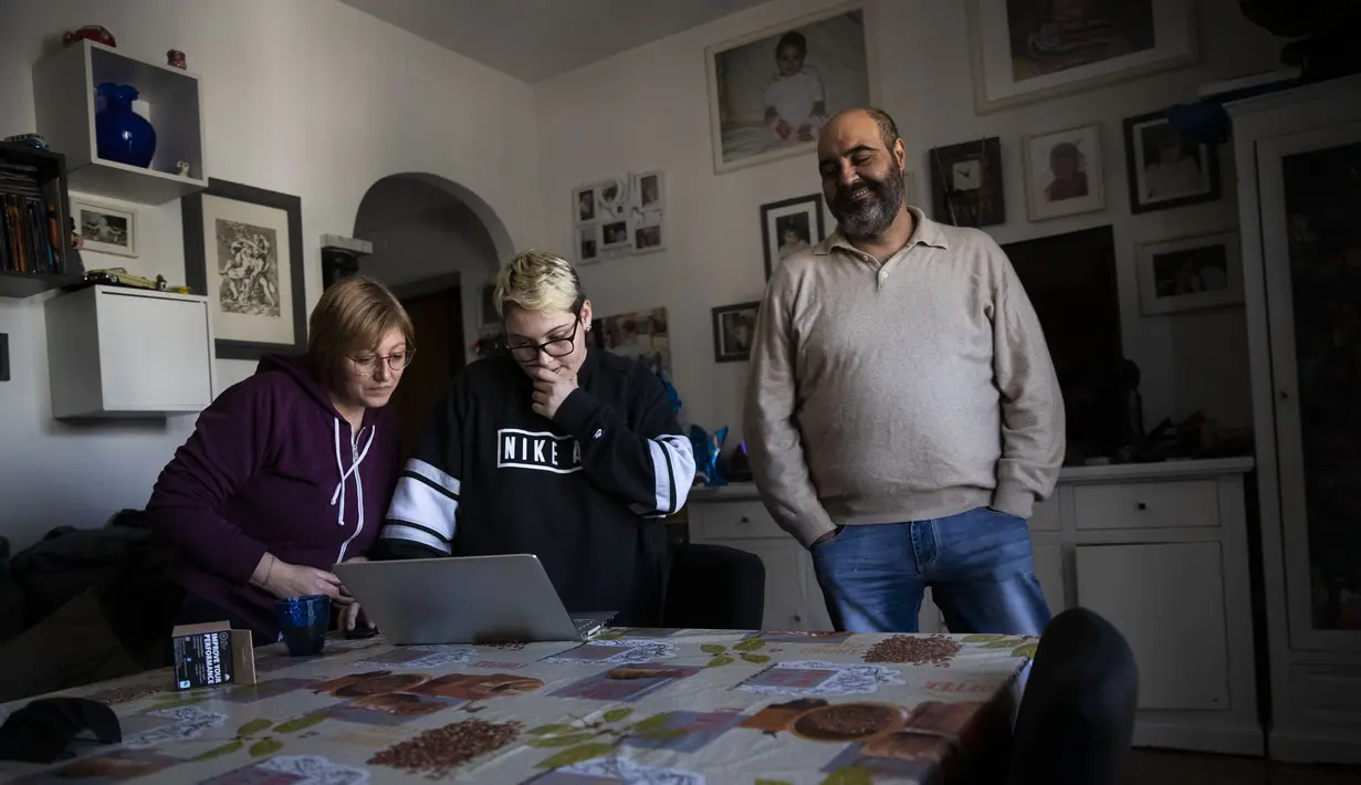 Matteo Coccimiglio diapit orang tuanya di dapur mereka di Roma, 20 Maret 2021. Sekolah tempat Matteo belajar bergabung dengan beberapa sekolah menengah di Italia yang memberikan siswa transgender hak untuk dikenal dengan nama selain yang diberikan saat mereka lahir. (AP Photo/Alessandra Tarantino)
