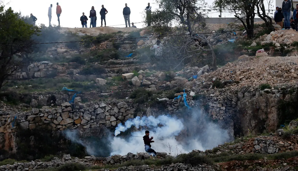 Seorang demonstran Palestina melempar balik tabung gas ke arah tentara israel saat terjadi bentrokan di kota Ramallah, Palestina (16/3). (AFP Photo/Abbas Momani)