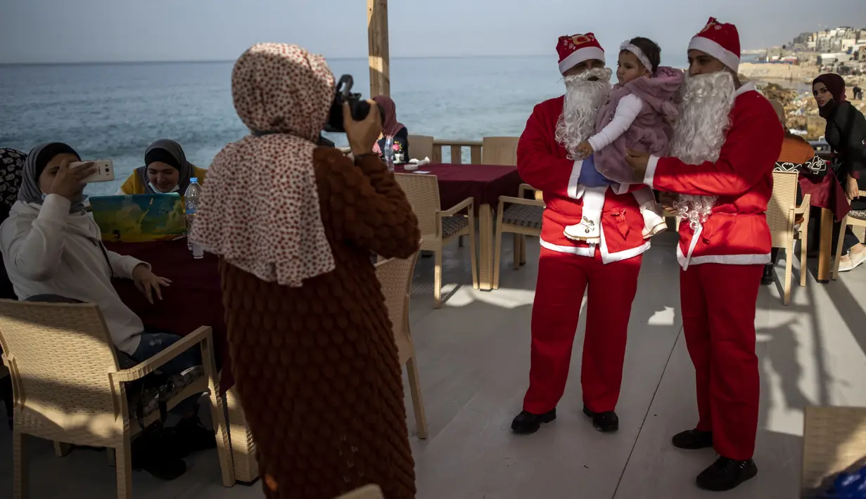 Pramusaji Palestina berpakaian Sinterklas menggendong seorang anak untuk berfoto di sebuah restoran di pantai di Kota Gaza, Minggu (13/12/2020). REstoran tersebut didandani dengan tema Natal, pelayanannya pun berpakaian seperti Sinterklas. (AP Photo/Khalil Hamra)