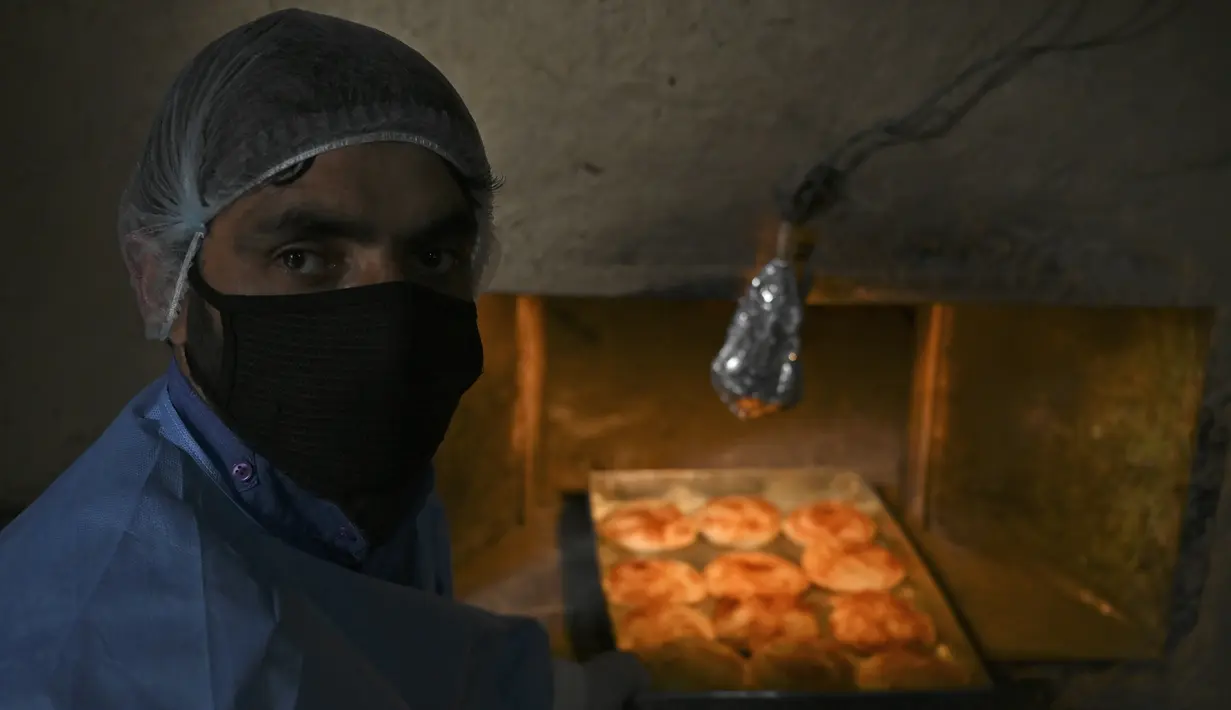 Pekerja mengeluarkan kue yang dipanggang dari oven di sebuah toko roti di Srinagar, India, Senin (18/5/2020). Toko roti tersebut melayani pengiriman untuk umat muslim yang merayakan Lebaran. (Tauseef MUSTAFA/AFP)