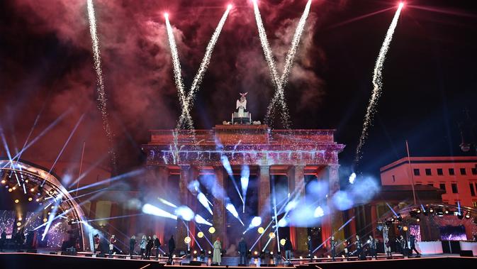 Musisi menyaksikan kembang api meledak di atas Gerbang Brandenburg yang terkenal di Berlin untuk mengantarkan tahun baru dalam konser selama Perayaan Tahun Baru di Berlin, Jerman, Jumat, 1 Januari 2021. (John MacDougall/Pool Photo via AP)