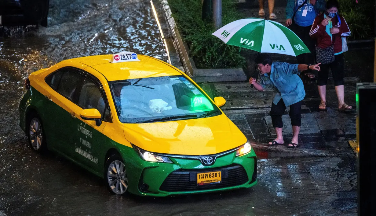 Seorang pejalan kaki menghentikan taksi saat hujan deras di Bangkok (23/9/2020). (AFP/Mladen Antonov)
