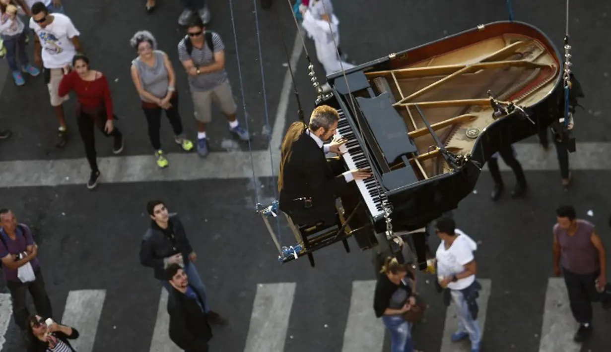 Sejumlah warga menyaksikan aksi Pianis Ricardo de Castro bermain piano di udara selama Virada Cultural di Brasil (22/6/2015). Virada Cultural merupakan acara budaya 24 jam tanpa gangguan dengan berbagai cara unik.  (AFP PHOTO/Miguel Schincariol)