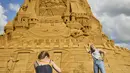 Orang-orang berpose dengan patung pasir tertinggi di dunia, yang sedang dibangun di Blokhus, Denmark, Rabu (7//2021). Memiliki ketinggian 21,16 meter, istana ini mengalahkan rekor dunia istana pasir tertinggi sebelumnya yang dipegang Jerman pada 2019. (Claus Bjoern Larsen/Ritzau Scanpix/AFP)