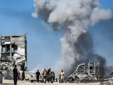 Orang-orang bergerak melewati bangunan yang hancur berlatar belakang kepulan asap menyusul serangan Israel di Jabalia, Jalur Gaza utara pada 25 Mei 2025. (Bashar TALEB/AFP)