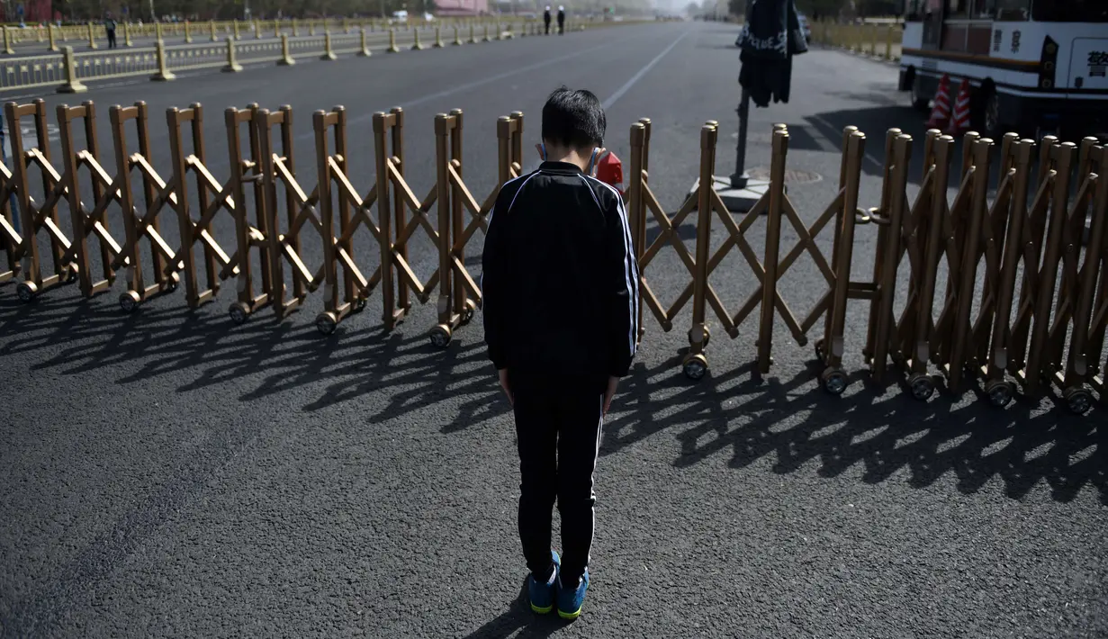 Seorang anak lelaki membungkuk di sebuah jalan dekat Lapangan Tiananmen selama peringatan nasional tiga menit untuk memperingati orang-orang yang meninggal dalam wabah virus coronavirus COVID-19, di Beijing (4/4/2020). (AFP/Greg Baker)
