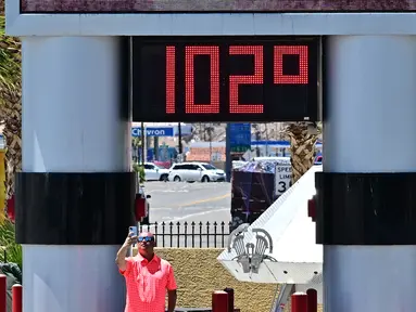 Seorang pria mengambil swafoto di samping termometer yang menunjukkan suhu 102 derajat celcius di Baker, California pada tanggal 11 Juli 2023, di tengah-tengah gelombang panas. (Photo by Frederic J. BROWN / AFP)