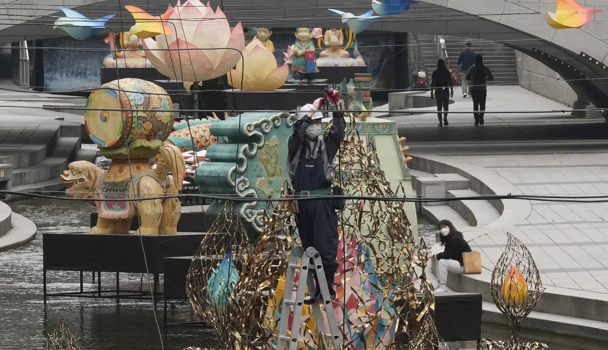 <p>Seorang pekerja mengenakan masker sebagai tindakan pencegahan terhadap penyebaran virus corona berdiri di tangga untuk mengatur kabel di dekat lentera untuk perayaan ulang tahun Buddha yang akan datang pada 8 Mei di Sungai Cheonggye di Seoul, Korea Selatan, Senin, 25 April 2022 (AP Photo/Ahn Young-joon)</p>