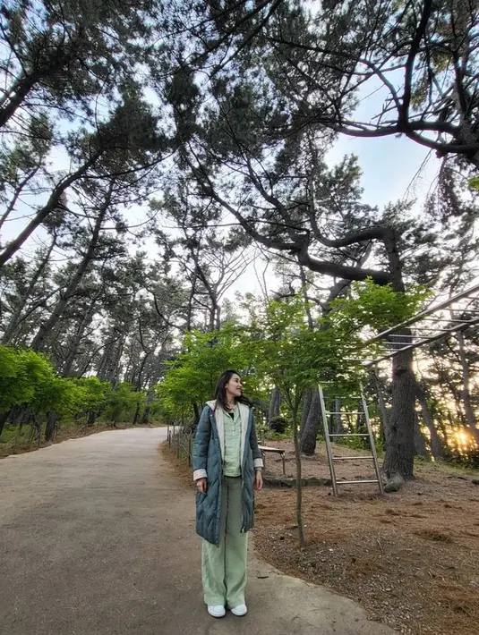 Outfit atas-bawah hijau tersebut juga dipasangkan dengan outerwear warna hijau tua. Terlihat menyatu dengan warna hijau di belakangnya lewat berbagai pepohonan. [Foto: @ayutingting92]