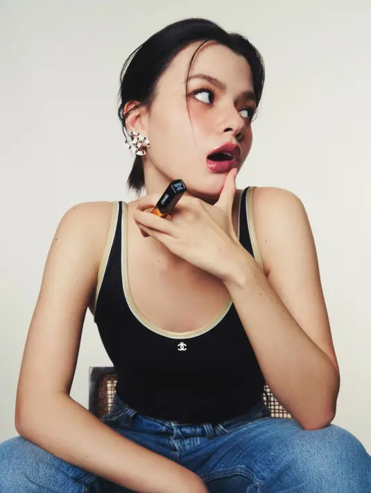 Dalam potret close-up yang memancarkan kepercayaan diri dan daya pikat, Becky tampil effortless mengenakan tank top hitam berlogo ikonik Chanel, dipadukan dengan jeans kasual dan aksesori statement berupa anting logam besar berbentuk logo “CC”. [Dok/CHANEL].