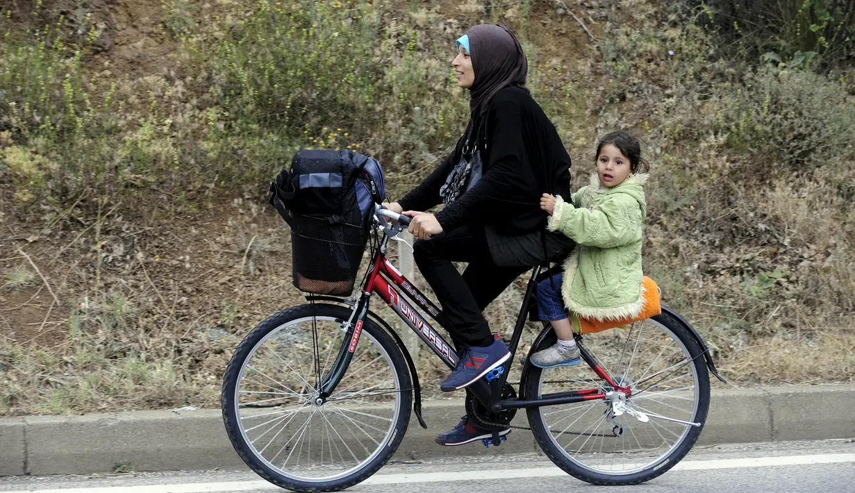 Seorang imigran Suriah menaiki sepeda bersama purtinya di dekat perbatasan Yunani di Makedonia, Rabu (17/6/2015). Mereka mencari perlindungan dengan menempuh ribuan kilometer. (REUTERS/Ognen Teofilovski)