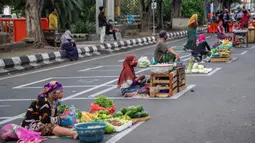 Pedagang menjual dagangannya di antara petak-petak untuk menerapkan jaga jarak (physical distancing) di sepanjang jalan di Surabaya, Selasa (2/6/2020). Garis petak-petak bagi pedagang itu sebagai langkah pencegahan penyebaran COVID-19. (Photo by Juni Kriswanto / AFP)