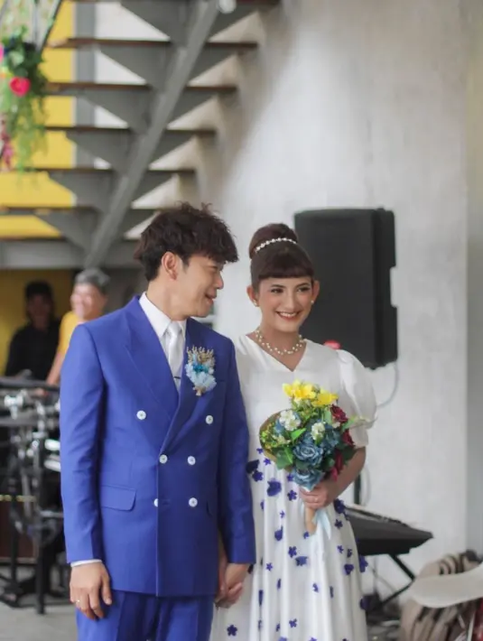 Qibil dengan setelan jas berwarna biru, sementara Qurrotu mengenakan dress putih dengan detail bunga-bunga warna biru. [Foto: IG/bahagia.wedding].