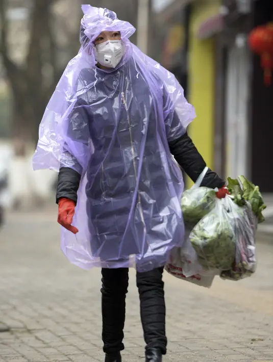 Seorang wanita mengenakan jas hujan dan masker membawa makanan di Wuhan di provinsi Hubei, China tengah, Senin, (10/2/2020). Angka kematian akibat virus corona di China meningkat lagi, dengan kematian hari Senin (10/2/2020) mencapai 908 orang, dengan adanya 97 kematian baru. (Chinatopix via AP)