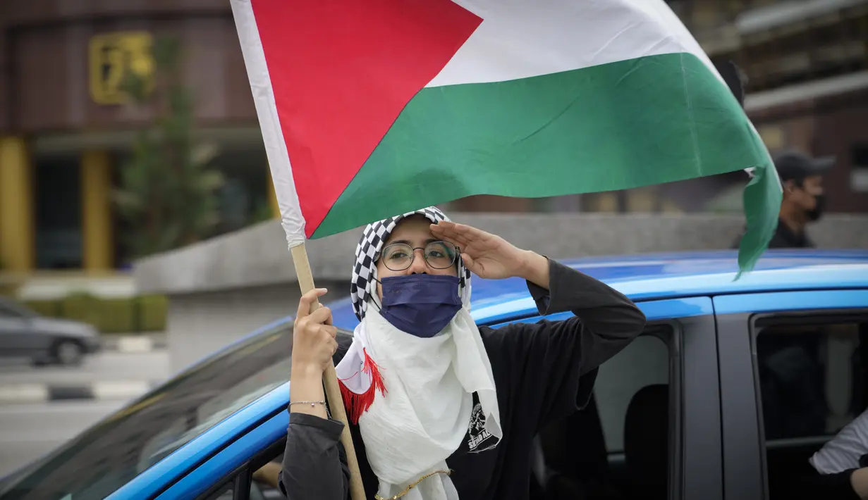 Seorang wanita Muslim memberi hormat dengan bendera Palestina saat konvoi protes menentang serangan Israel di Gaza di luar Kedutaan Besar Amerika Serikat di Kuala Lumpur, Malaysia, Jumat (21/5/2021).  (AP Photo / Vincent Thian)