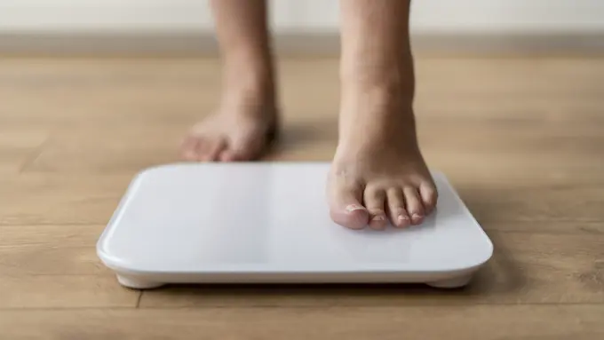 Sebelah kaki seorang perempuan sedang menginjak timbangan badan (Foto Dok: Freepik/freepik)