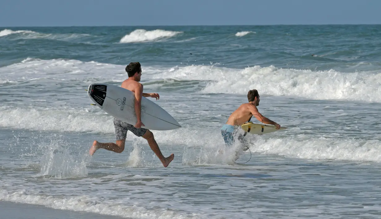 Peselancar berlari ke ombak ketika pantai dibuka di Jacksonville Beach, Florida (17/4/2020). Pengumuman DeSantis pada hari Jumat datang ketika pantai Florida utara menjadi yang pertama yang memungkinkan pengunjung pantai untuk kembali sejak penutupan.  (Will Dickey/The Florida Times-Union via AP)