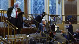 Orang-orang berlindung dalam galeri House saat pengunjuk rasa mencoba masuk ke House Chamber di Gedung Capitol Hill, Washington DC, Amerika Serikat, Rabu (6/1/2021). Kericuhan terjadi saat massa pendukung Donald Trump merangsek masuk ke dalam Gedung Capitol Hill. (AP Photo/Andrew Harnik)