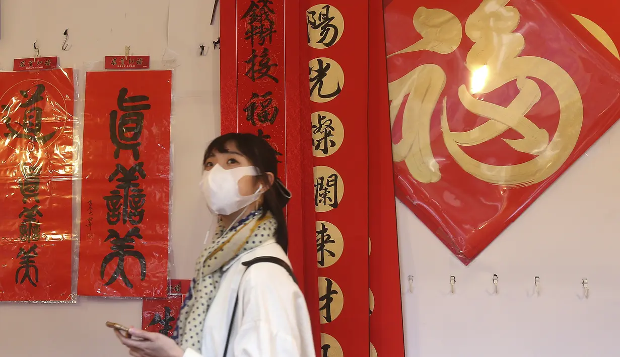 Seorang wanita memakai masker untuk mencegah penyebaran virus corona berjalan melalui lorong-lorong yang dihias dekorasi Imlek di sepanjang pasar Jalan Dihua di Taipei, Taiwan, Rabu (10/2/2021).  (AP Photo/Chiang Ying-ying)