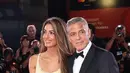 Amal Clooney tampil memukau mengenakan gaun kuning muda dari Atelier Versace, dipadukannya dengan tas tangan dari Judith Leiber.