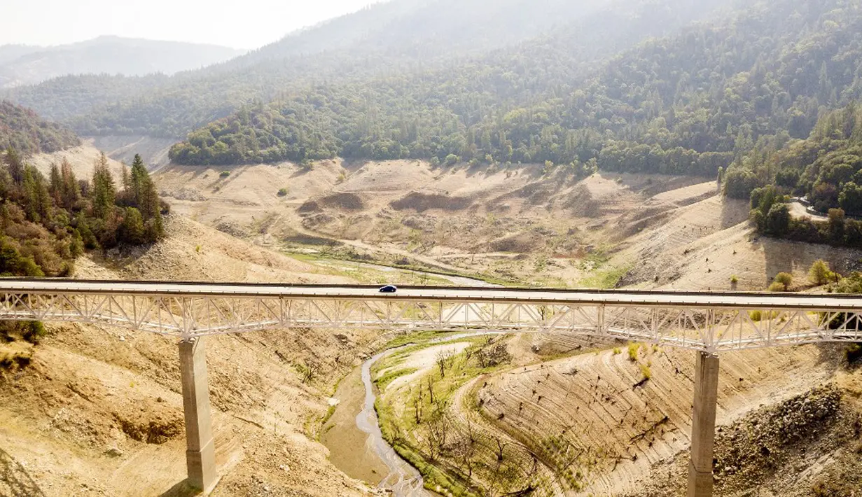 Sebuah mobil melaju di sepanjang Enterprise Bridge saat melewati Danau Oroville di Oroville, California, Amerika Serikat, 5 September 2021. Sebagian besar California dilanda panas berlebihan, kekeringan parah, dan serangkaian kebakaran hutan besar-besaran. (JOSH EDELSON/AFP)