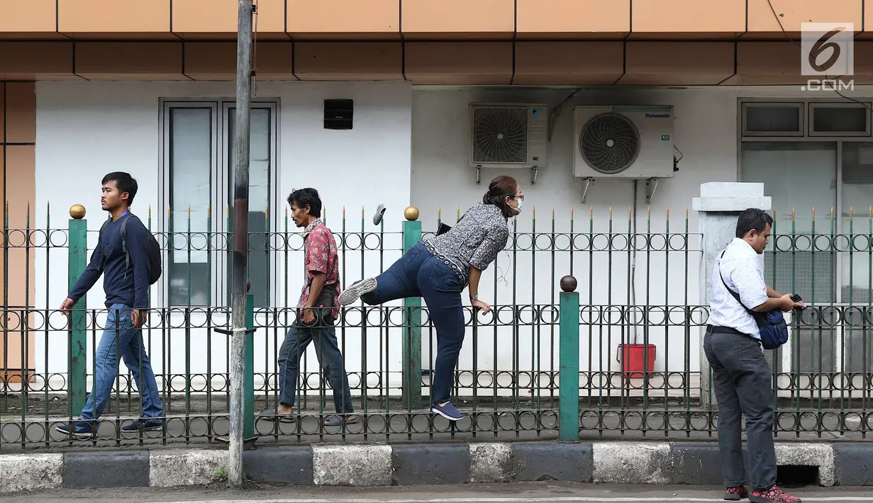 Penumpang menaiki pagar pembatas untuk keluar dari Stasiun Cikini di Jakarta, Jumat (22/3). Jauhnya akses pintu masuk dan keluar stasiun menyebabkan sebagian orang mempersingkat waktu dengan melompat pagar pembatas. (Liputan6.com/Immanuel Antonius)