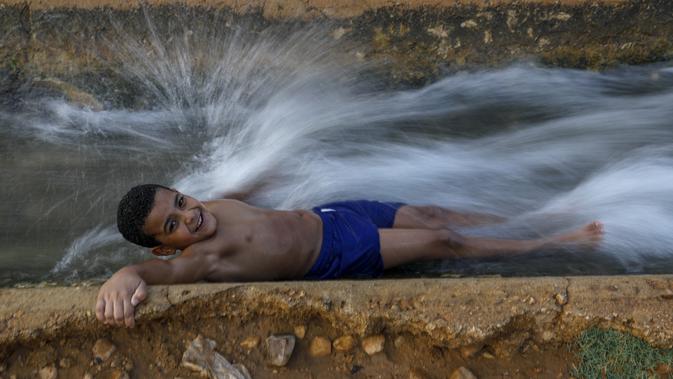 Seorang anak bermain di aliran mata air yang digunakan untuk irigasi untuk mendinginkan tubuh saat suhu udara mencapai 44 derajat Celcius di kota Jericho, Tepi Barat (1/9/2020). (AFP Photo/Ahmad Gharabli)