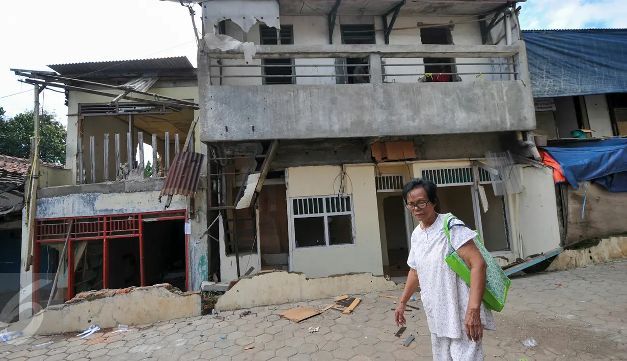 Seorang ibu melintas di depan rumah yang tengah dibongkar, tepat di samping Kantor Kelurahan Rawajati, Pancoran, Jakarta, Selasa (22/12). Empat rumah petak dibongkar Satpol PP karena berdiri di atas lahan milik Pemprov DKI. (Liputan6.com/Yoppy Renato)