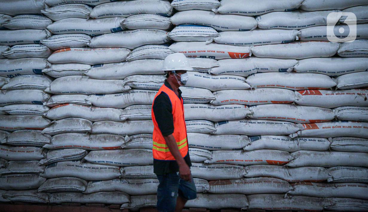 Pekerja melintas di depan tumpukan beras milik Perum Bulog di kawasan Pulo Mas, Jakarta, Kamis (26/11/2020). Kementan kembali memastikan bahwa meski tengah dilanda pandemi Covid-19 pasokan beras hingga akhir tahun masih ada stok beras sebanyak 7,1 juta ton. (Liputan6.com/Faizal Fanani)