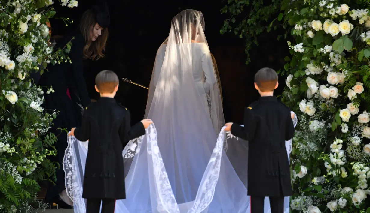 Dua bocah memegang gaun putih panjang Meghan Markle saat akan melangsungkan upacara pernikahan dengan Pangeran Harry di St George's Chapel, Kastil Windsor, Windsor, Inggris, Sabtu (19/5). (Andrew Matthews/POOL/AFP)