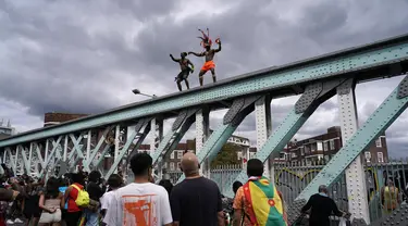 Orang-orang yang bersuka ria menari di atas jembatan kereta api selama Karnaval Notting Hill tahunan di London barat, Senin (29/8/2022). Karnaval yang kembali ke jalanan untuk pertama kalinya dalam dua tahun, setelah digagalkan oleh pandemi, adalah salah satu perayaan festival terbesar dari jenisnya di Eropa. (AP Photo/Alberto Pezzali)