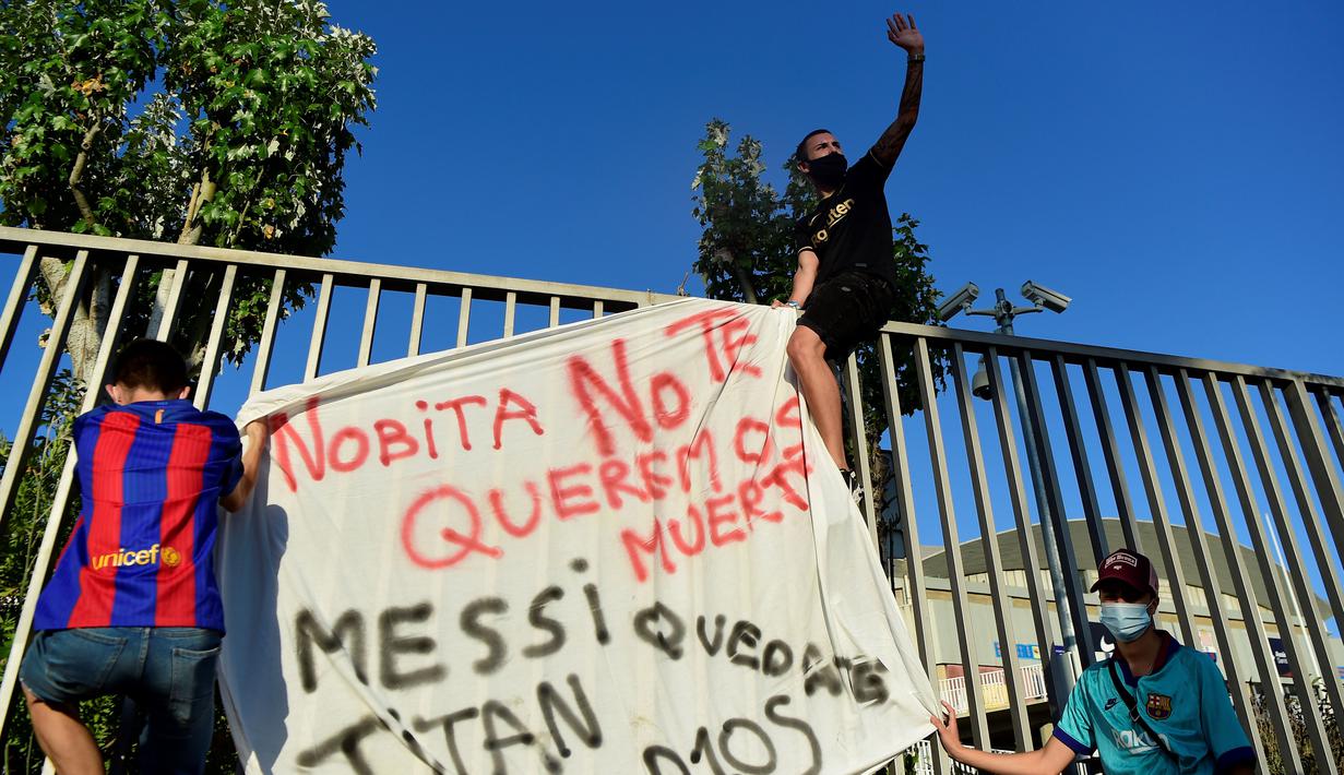 Suporter memanjat pagar dan memasang spanduk saat protes di depan kantor Barcelona, Rabu (26/8/2020). Dalam aksi tersebut fans meminta Lionel Messi bertahan dan menuntut Josep Maria Bartomeu mundur dari jabatannya. (AFP/Pau Barrena)