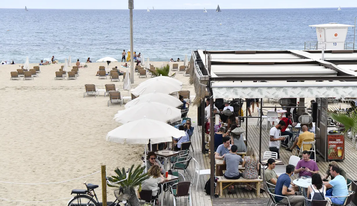 Orang-orang duduk di bar teras di Pantai Bogatell di Barcelona, Minggu (6/6/2021). Spanyol akan mengizinkan semua pelancong yang divaksinasi untuk mengunjungi negara itu mulai 7 Juni, dengan tujuan kembali menghidupkan industri perjalanan yang terpukul pandemi Covid-19. (Pau BARRENA/AFP)