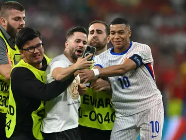 Petugas keamanan menghentikan penyerbu lapangan saat ia mengambil swafoto dengan Kylian Mbappe pada semifinal Euro 2024 antara Spanyol vs Prancis di Allianz Arena, Rabu (10/7/2024) dini hari WIB. (Fabrice COFFRINI / AFP)