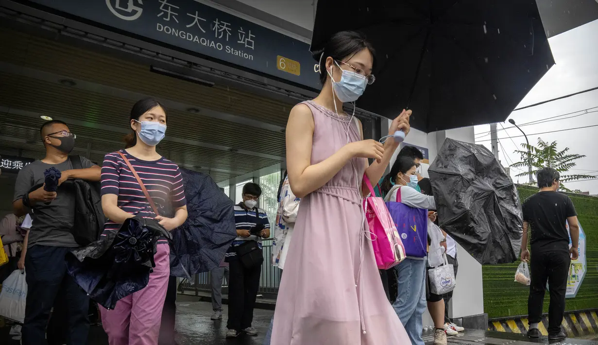 <p>Para penumpang bermasker dan membawa payung berjalan keluar dari stasiun kereta bawah tanah pada jam sibuk pagi hari pada hari hujan di Beijing, Rabu (29/6/2022). Pemerintah China mengurangi masa karantina wajib untuk pelancong yang merupakan pelonggaran pertama yang diterapkan negara itu kepada turis sejak Covid-19 merebak. (AP Photo/Mark Schiefelbein)</p>