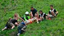 Seorang pria ditandu setelah ambil bagian dalam kompetisi Cheese Rolling (mengejar keju) di Bukit Cooper, Gloucestershire, Inggris, Senin (27/5/2019). Festival ini sebenarnya cukup berbahaya, sehingga tidak heran jika setiap tahun selalu ada korban yang luka. (Ben Birchall/PA via AP)