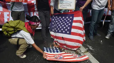 Aktivis membakar bendera AS dengan wajah Presiden terpilih Donald Trump di depan kedutaan AS, Manila, Filipina (20/1). Pengunjuk rasa menuding Presiden terpilih AS itu memiliki sifat seksisme, rasisme dan xenophobia. (AFP Photo/Ted Aljibe)