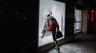 Seorang pendemo memasuki toko melalui jendela yang rusak di New York, AS (1/6/2020). Sejumlah toko di Amerika Serikat dijarah oleh pendemo yhang mengecam kematian warga kulit hitam George Floyd. (Foto AP / Frank Franklin II)