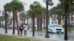 Orang-orang berjalan di sepanjang Ocean Boulevard di tengah hujan di Pantai Myrtle, Carolina Selatan (3/8/2020). Badai Isaias terus bergerak ke utara di sepanjang pesisir timur AS. (Sean Rayford/Getty Images/AFP)