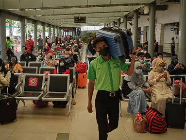 Petugas membawa koper melewati calon penumpang yang sedang menunggu keberangkatan kereta di Stasiun Pasar Senen, Jakarta, Jumat (24/12/2021). H-1 libur Natal dan Tahun Baru, peningkatan penumpang kereta jarak jauh mulai terlihat dengan tujuan sejumlah kota di Pulau Jawa. (Liputan6.com/Faizal Fanani)