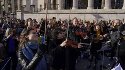 Anggota orkestra bermain sebagai bagian dari demonstrasi anti-perang menyusul serangan Rusia terhadap Ukraina di Trafalgar Square, London, Minggu (6/3/2022).  Flashmob yang terdiri dari 200 musisi klasik itu untuk menunjukkan dukungan terhadap Ukraina setelah invasi Rusia. (AP Photo/Alberto Pezzali)