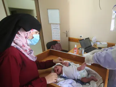 Seorang petugas medis yang mengenakan alat pelindung diri memeriksa seorang bayi di sebuah pusat layanan kesehatan saat pemberlakuan lockdown di Kota Rafah, Jalur Gaza, 9 September 2020. (Xinhua/Khaled Omar)