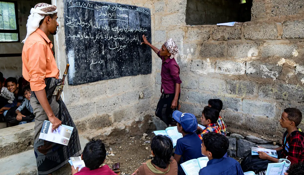 Seorang guru mengajar anak-anak dalam kelas agama di tempat terbuka di luar gedung yang sudah rapuh yang menjadi sekolah darurat di Mokha, provinsi barat Yaman, Taiz, pada 27 Agustus 2024. (Khaled ZIAD/AFP)